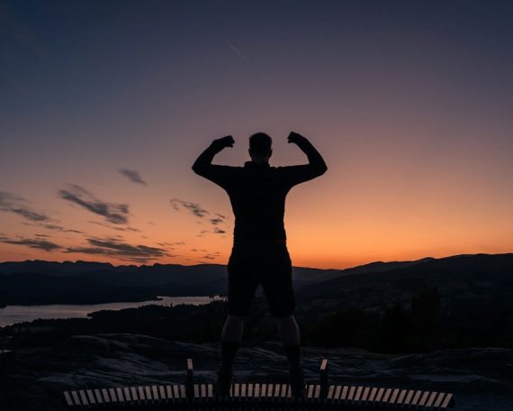 a man standing on top of a bench at sunset